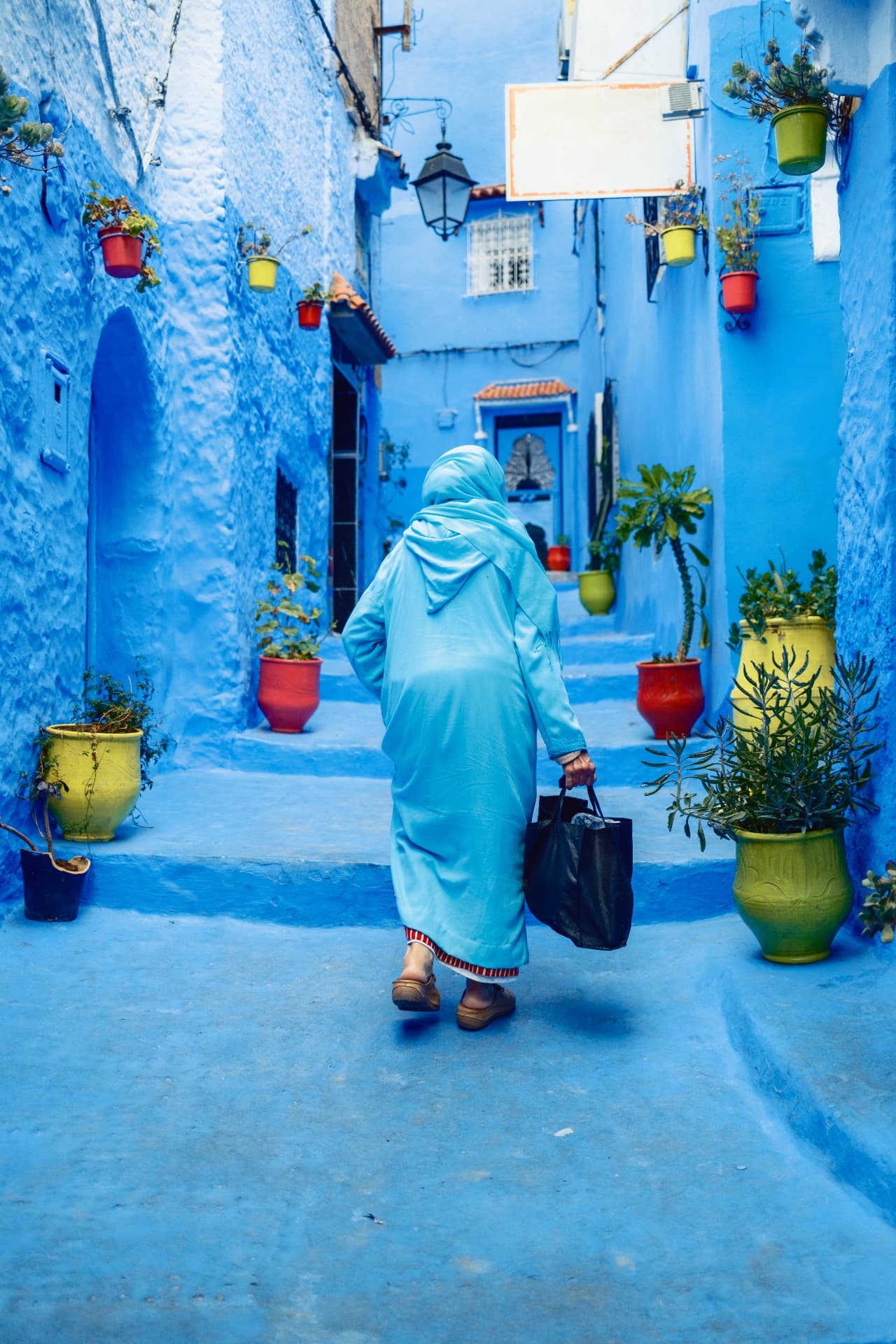 Person in a blue robe walking through the blue streets of Chefchaouen