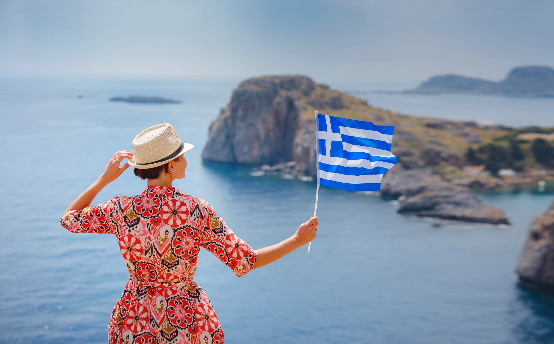 Traveler waving a Greek flag above the Aegean coastline